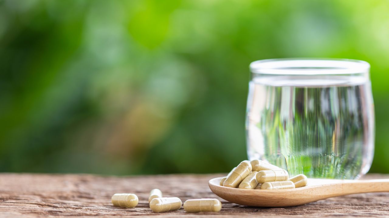 Herbal colon cleanse capsules on wooden spoon with glass of water and green natural background