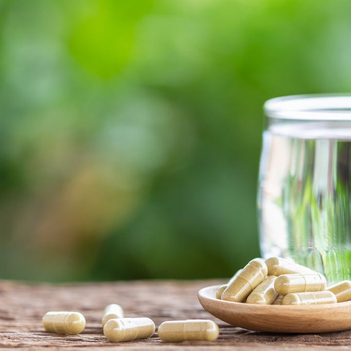Herbal colon cleanse capsules on wooden spoon with glass of water and green natural background