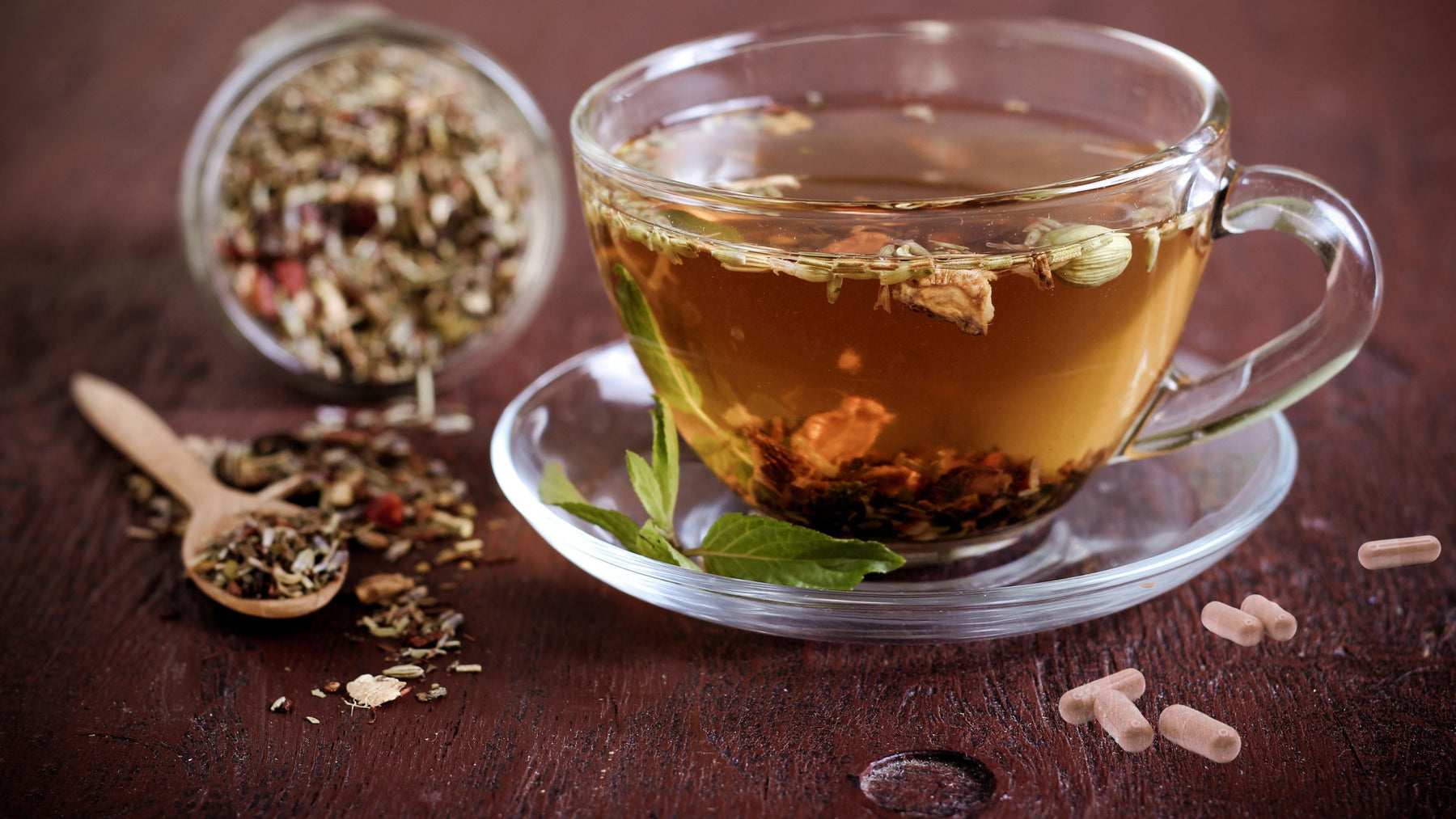 Herbal colon cleanse tea in glass cup with loose herbs and capsules on dark wooden table
