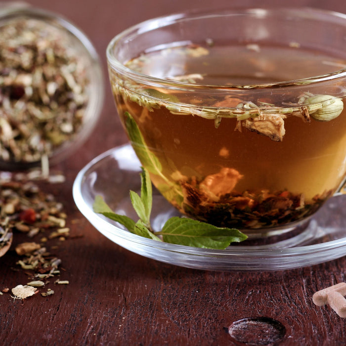 Herbal colon cleanse tea in glass cup with loose herbs and capsules on dark wooden table
