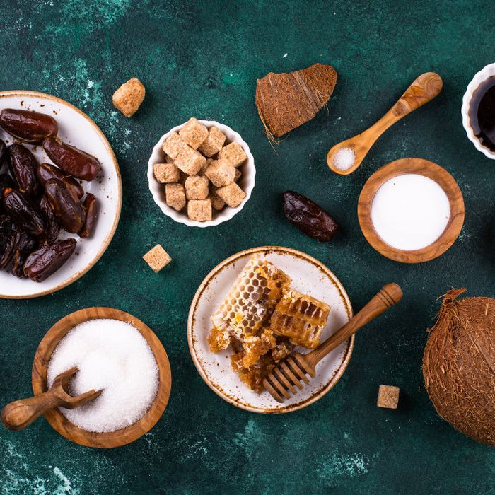 Natural sweetener varieties including dates, coconut sugar, honey, brown sugar and white sugar on dark green background