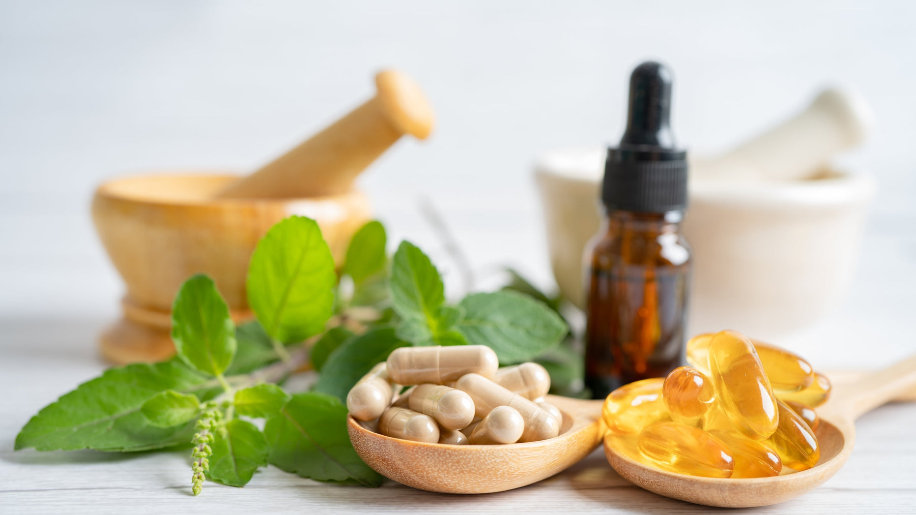 Herbal cleanse supplements including capsules, tincture drops and fresh herbs with mortar and pestle on white background