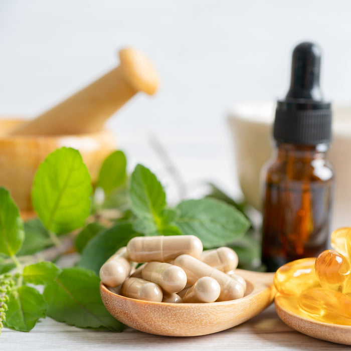 Herbal cleanse supplements including capsules, tincture drops and fresh herbs with mortar and pestle on white background