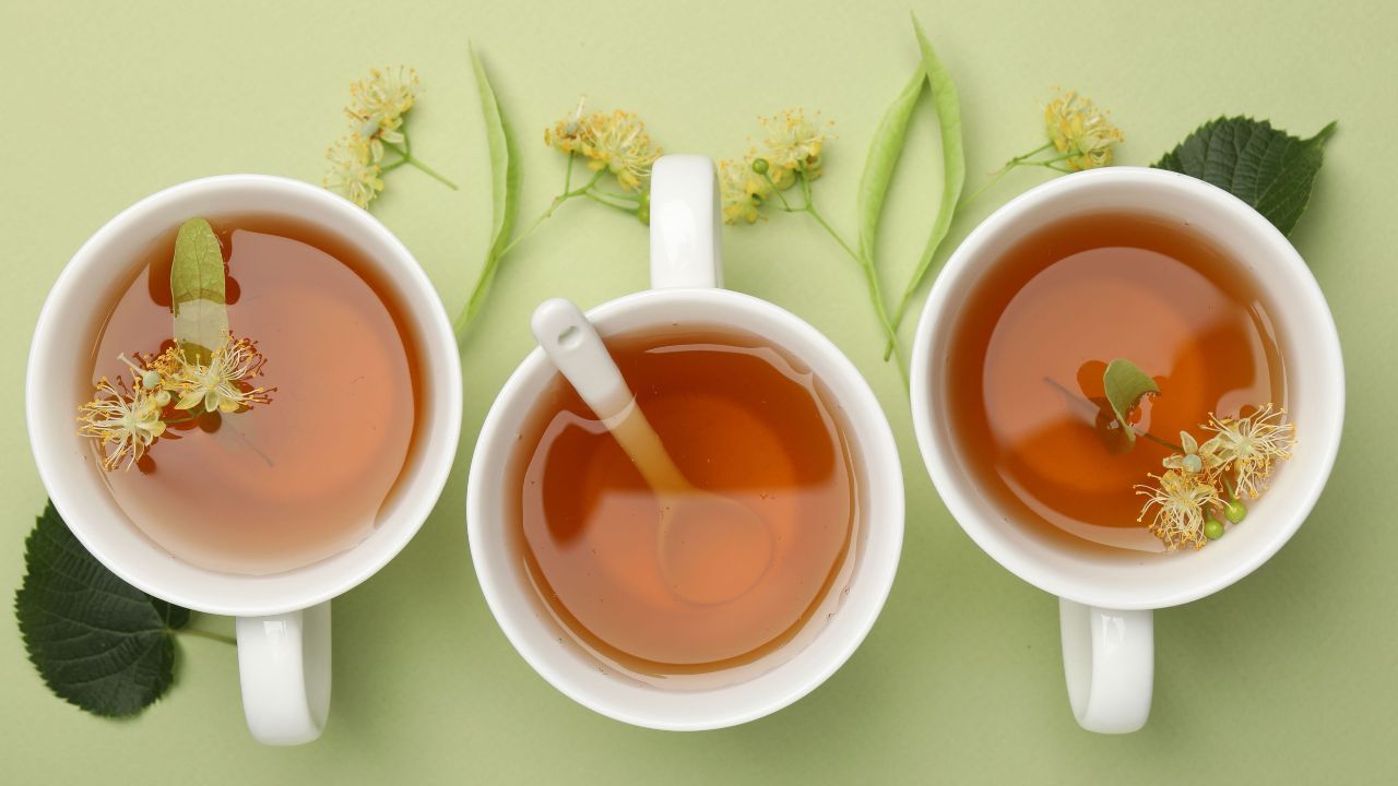 Three cups of herbal tea with linden flowers on green background - SpeedyVite colon cleanse support