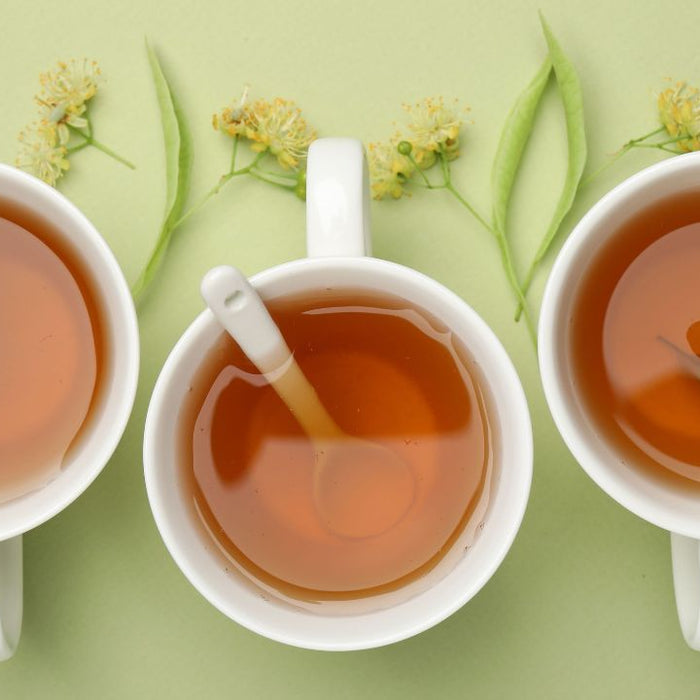 Three cups of herbal tea with linden flowers on green background - SpeedyVite colon cleanse support
