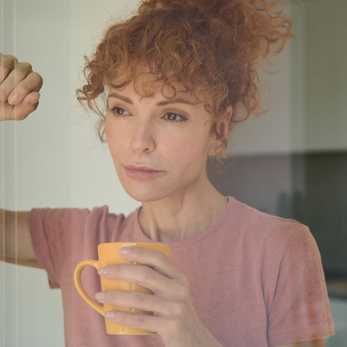 Thoughtful woman in a pink t-shirt holding an orange mug beside a window
