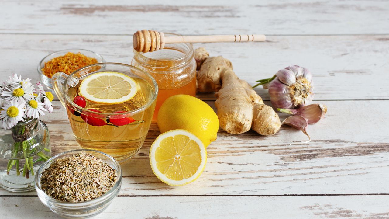 Herbal immune support ingredients including tea, honey, ginger, garlic, chamomile and lemon on white wood background