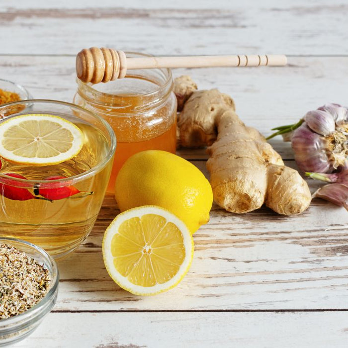 Herbal immune support ingredients including tea, honey, ginger, garlic, chamomile and lemon on white wood background