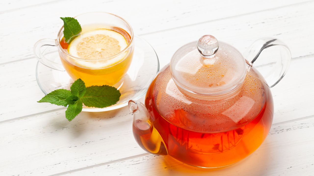 Glass teapot of herbal kidney cleanse tea with lemon slice and fresh mint leaves on white background