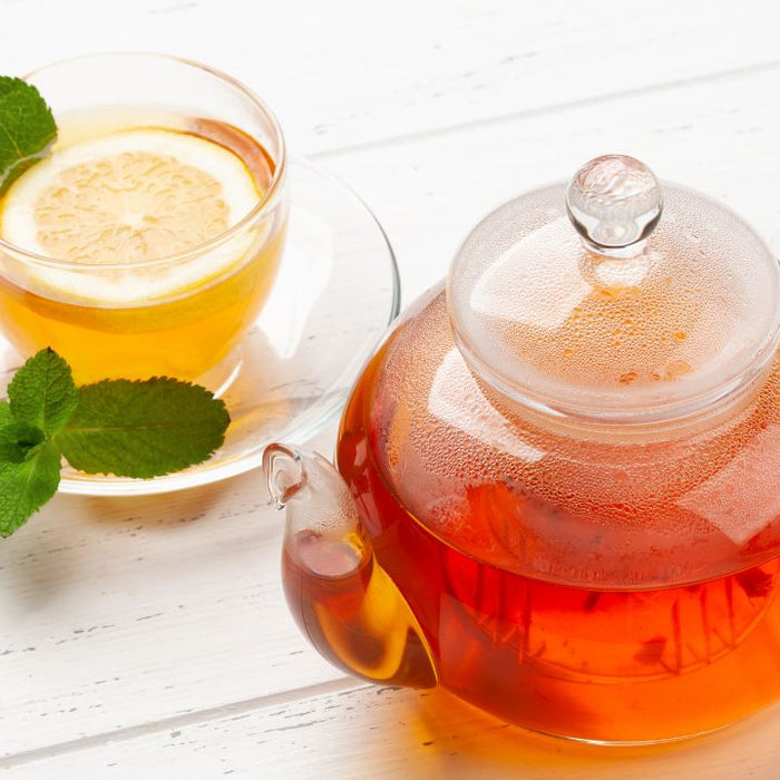Glass teapot of herbal kidney cleanse tea with lemon slice and fresh mint leaves on white background
