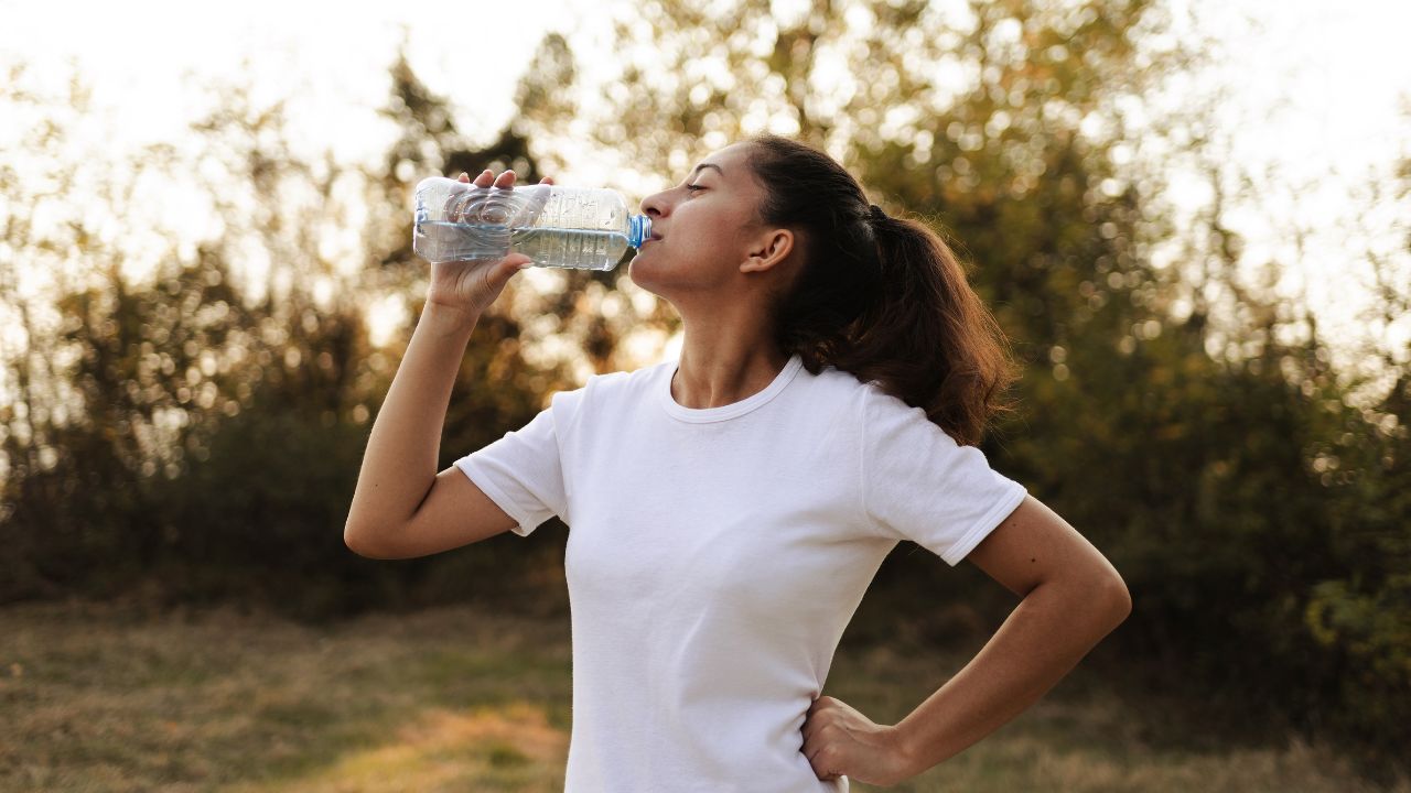 Woman drinking water outdoors as part of a natural kidney health and hydration wellness routine