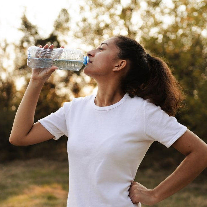 Woman drinking water outdoors as part of a natural kidney health and hydration wellness routine