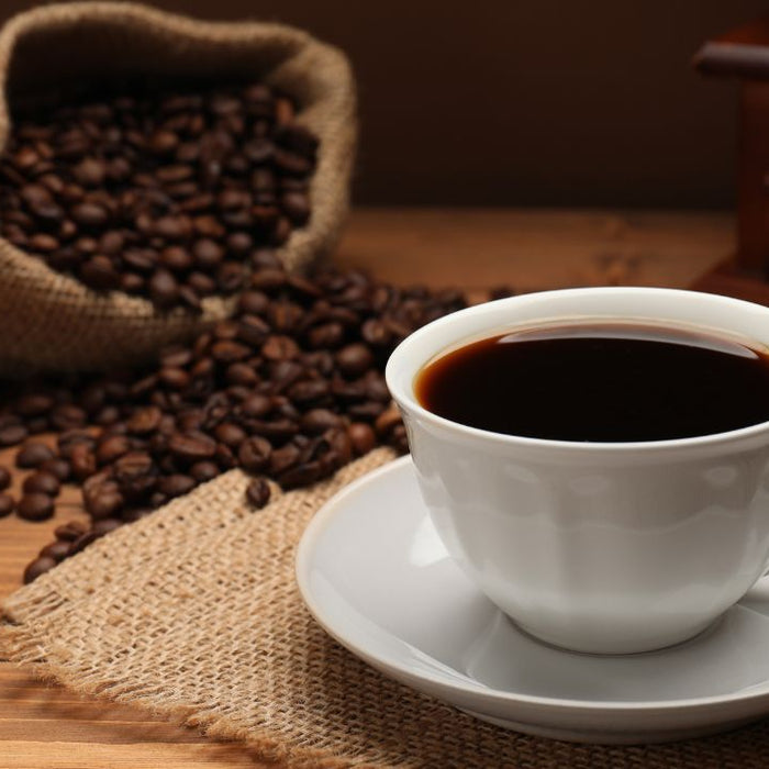 Black coffee in white cup with spilled coffee beans on wooden table