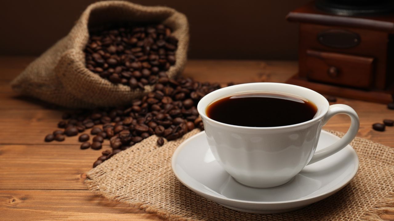 Black coffee in white cup with spilled coffee beans on wooden table