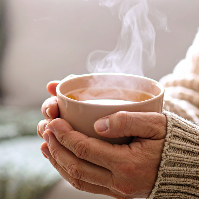 Hands in a cozy knit sweater holding a steaming mug of herbal tea