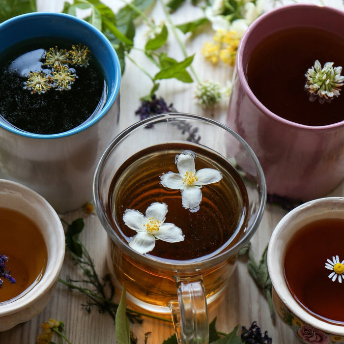 Five cups of different herbal teas with fresh flowers and herbs showing variety of vitamins and nutrients in herbal tea