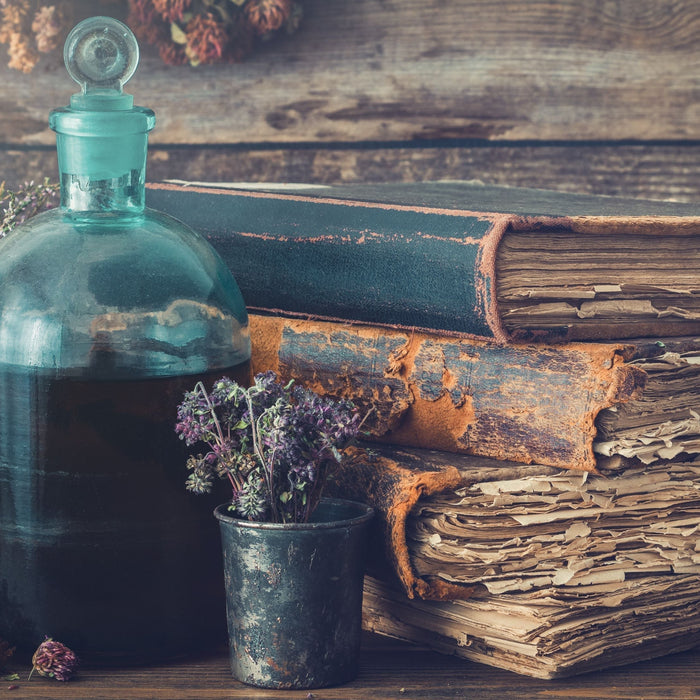Antique apothecary bottle with herbal tincture alongside old leather books dried herbs and mortar and pestle representing centuries of Swedish Bitters tradition