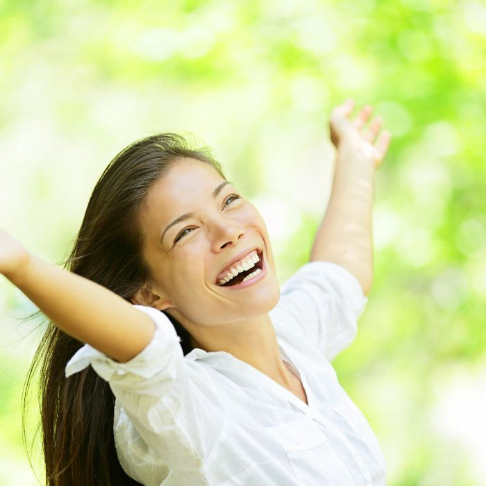 Woman outdoors in summer sunshine with arms raised among green trees